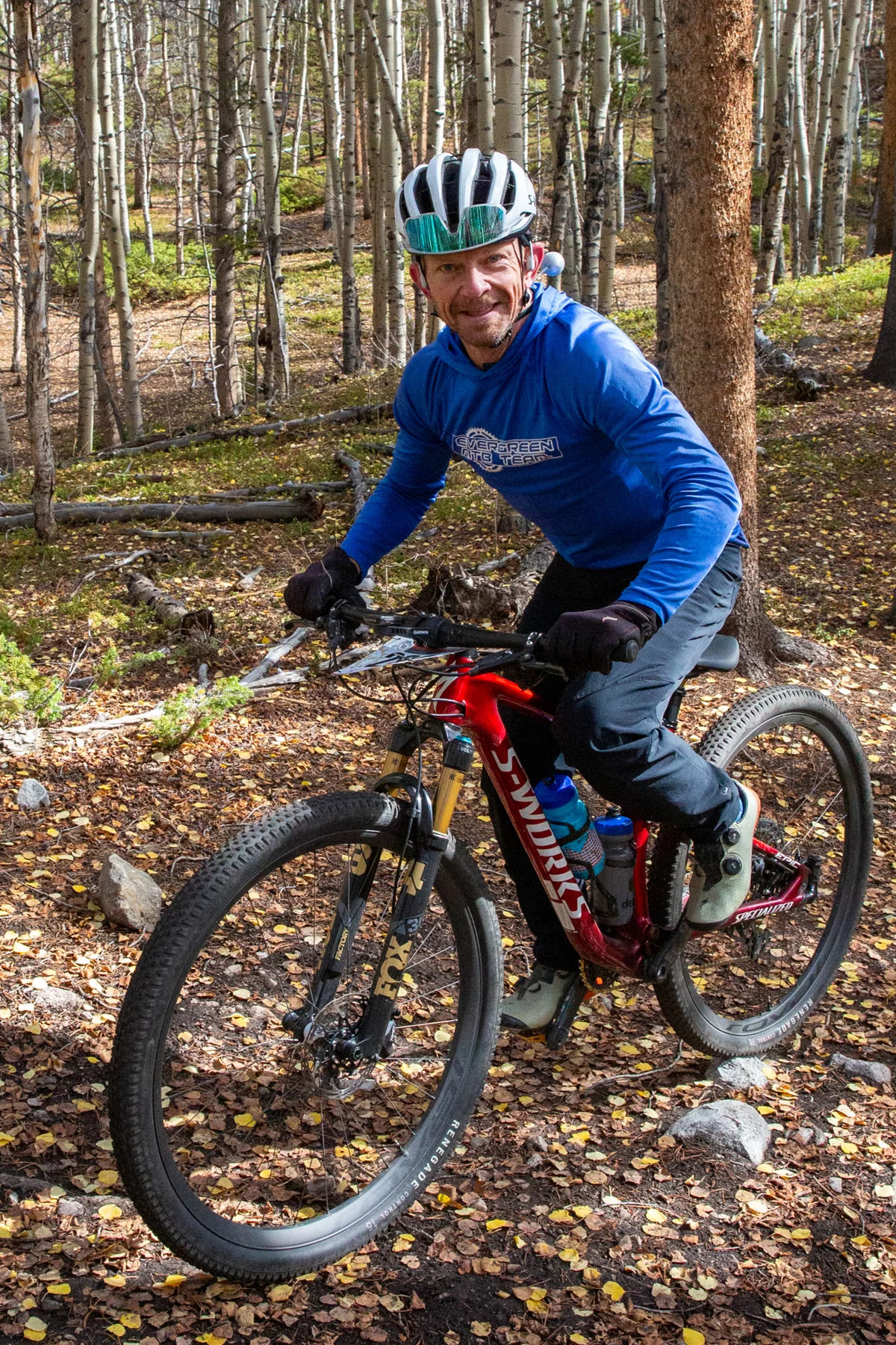 A smiling cyclist in a blue top rides a red mountain bike through aspens.