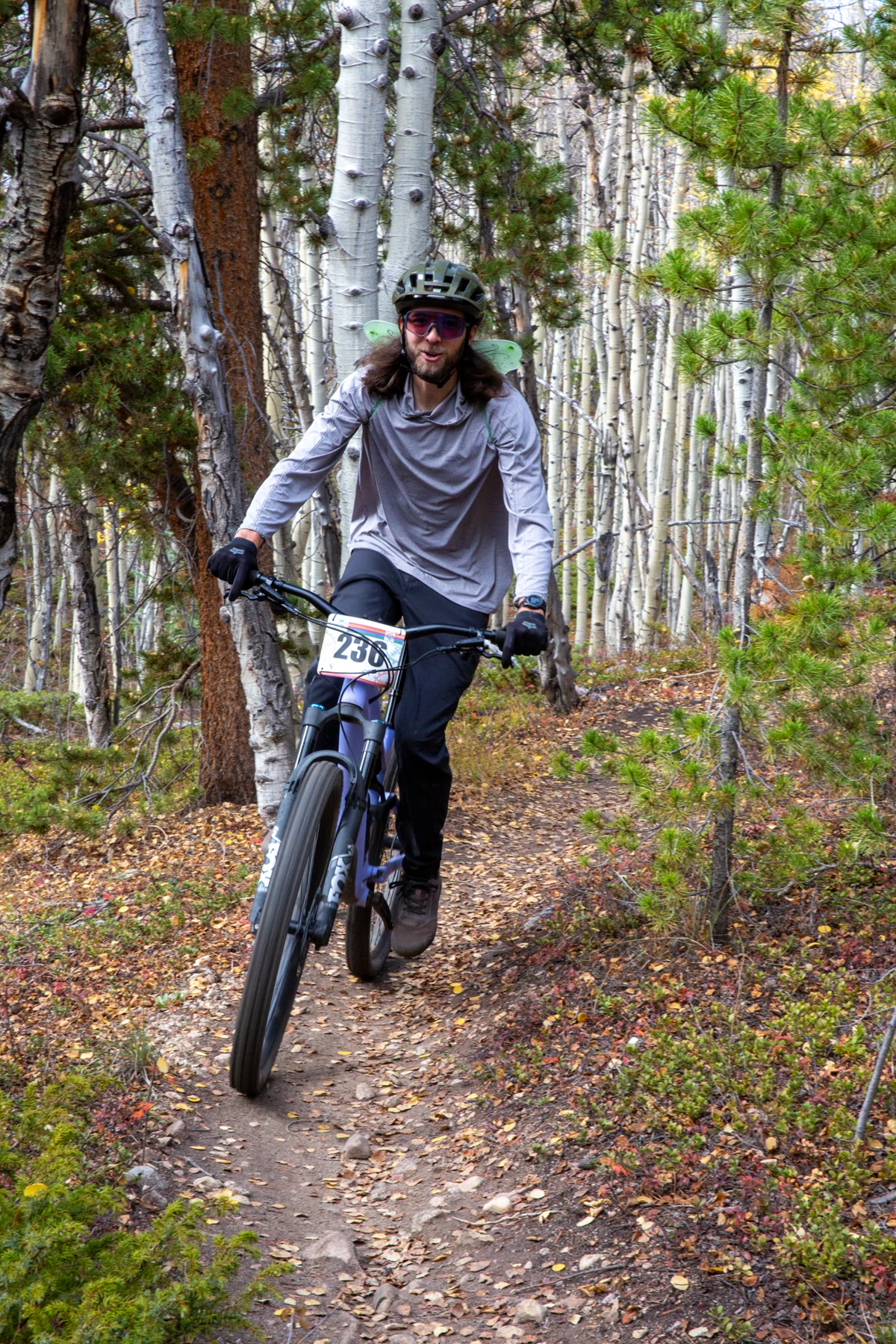A cyclist wearing fairy wings rides toward the camera on an aspen-lined trail.