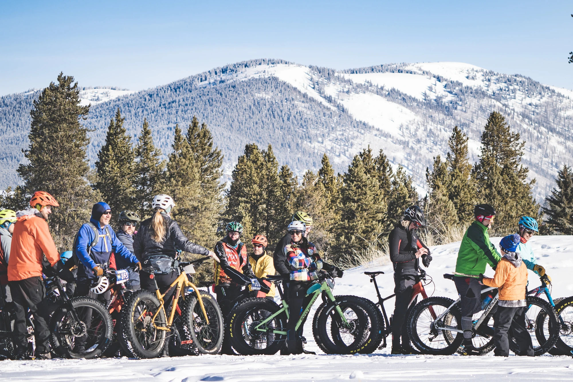Colorado Cup participants gather with fat bikes on snow, with a broad mountain backdrop.