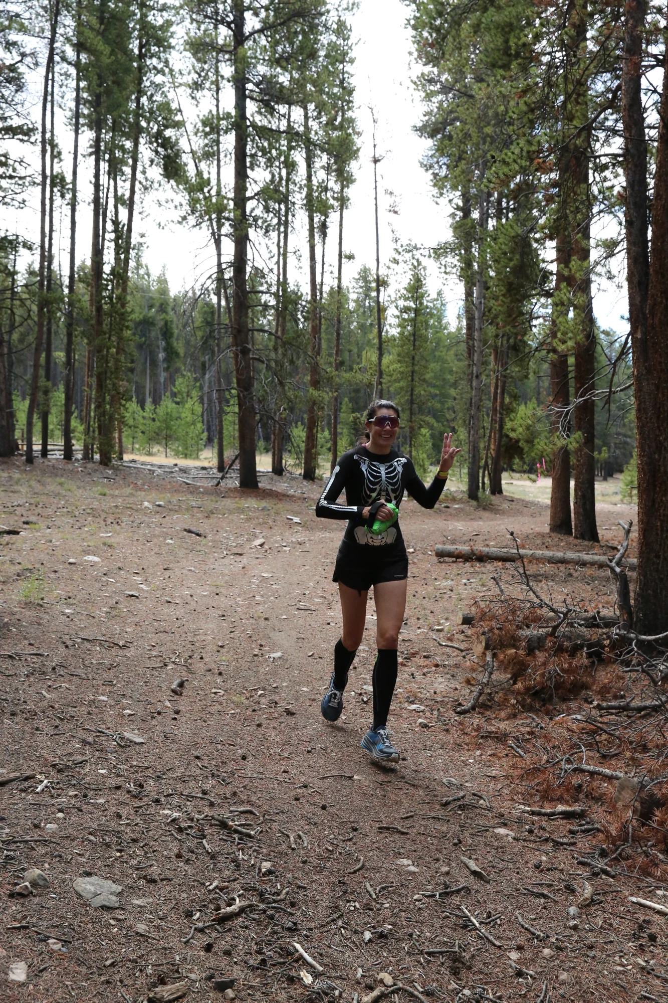 A participant in black runs along the wooded course and waves at the camera.