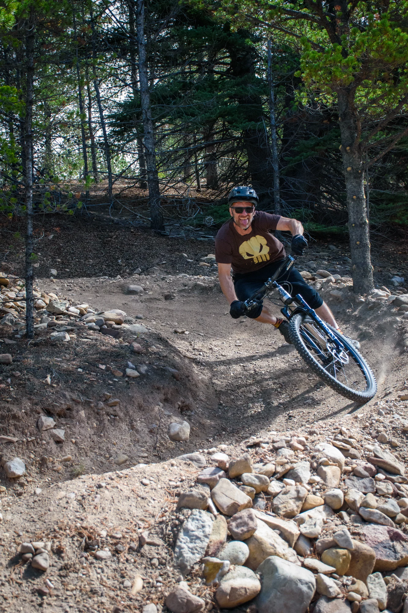 A smiling cyclist rounds a rocky berm in the forest.