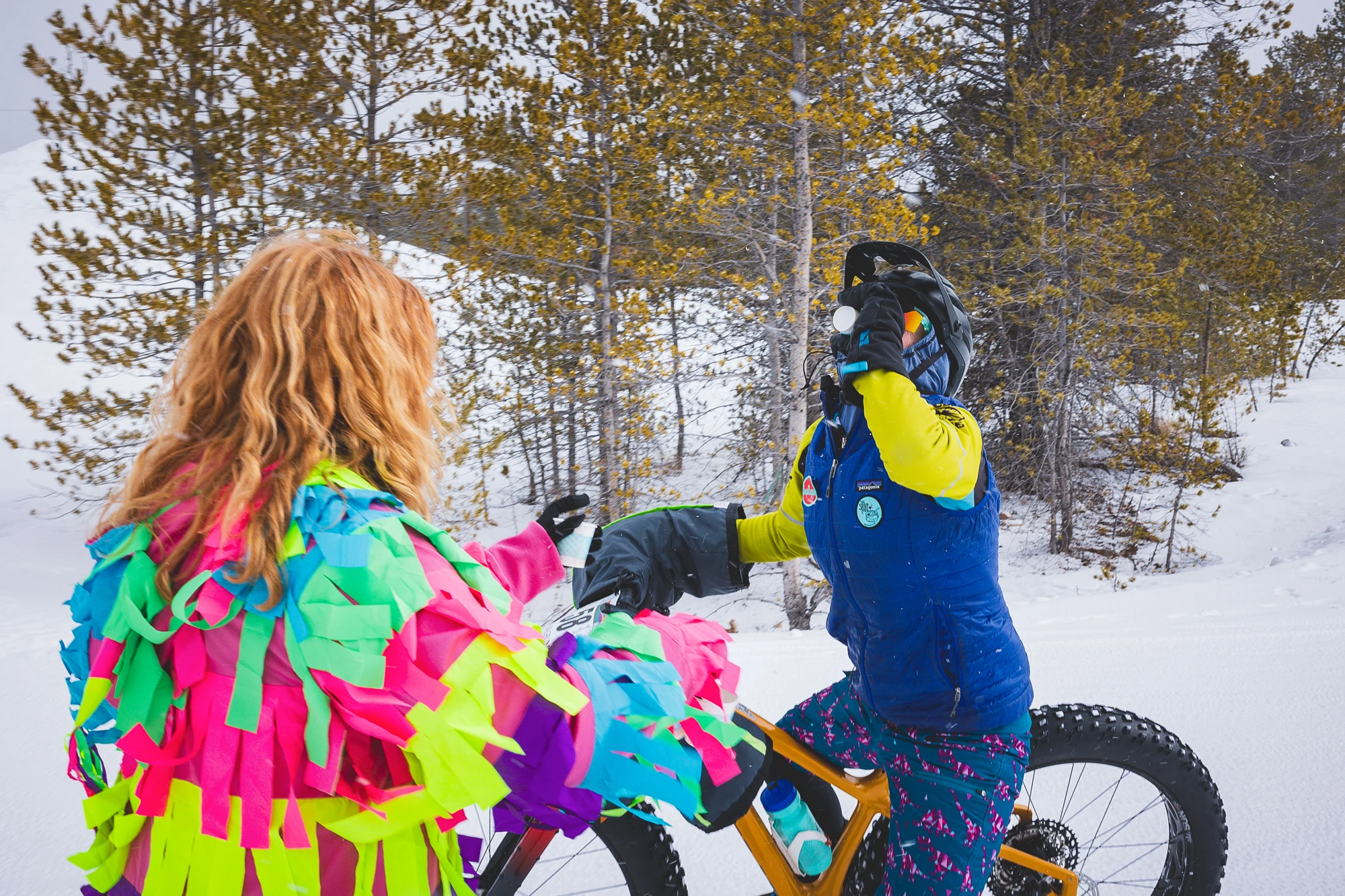 Two brightly costumed cyclists celebrating beside fat bikes in snow.